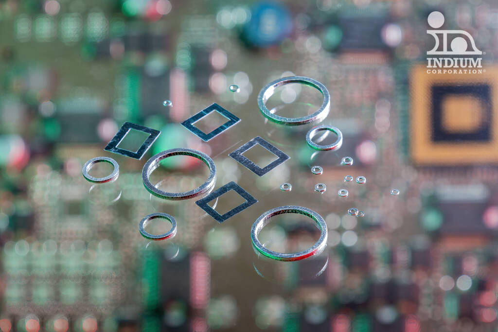 Close-up of metal rings and solder preform washers on a circuit board with a blurred background and a logo in the top right corner.