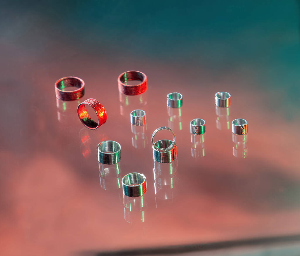 Several shiny rings, some red and some silver, placed on a reflective surface with a colorful background, resembling the precision of soldering tube craftsmanship.