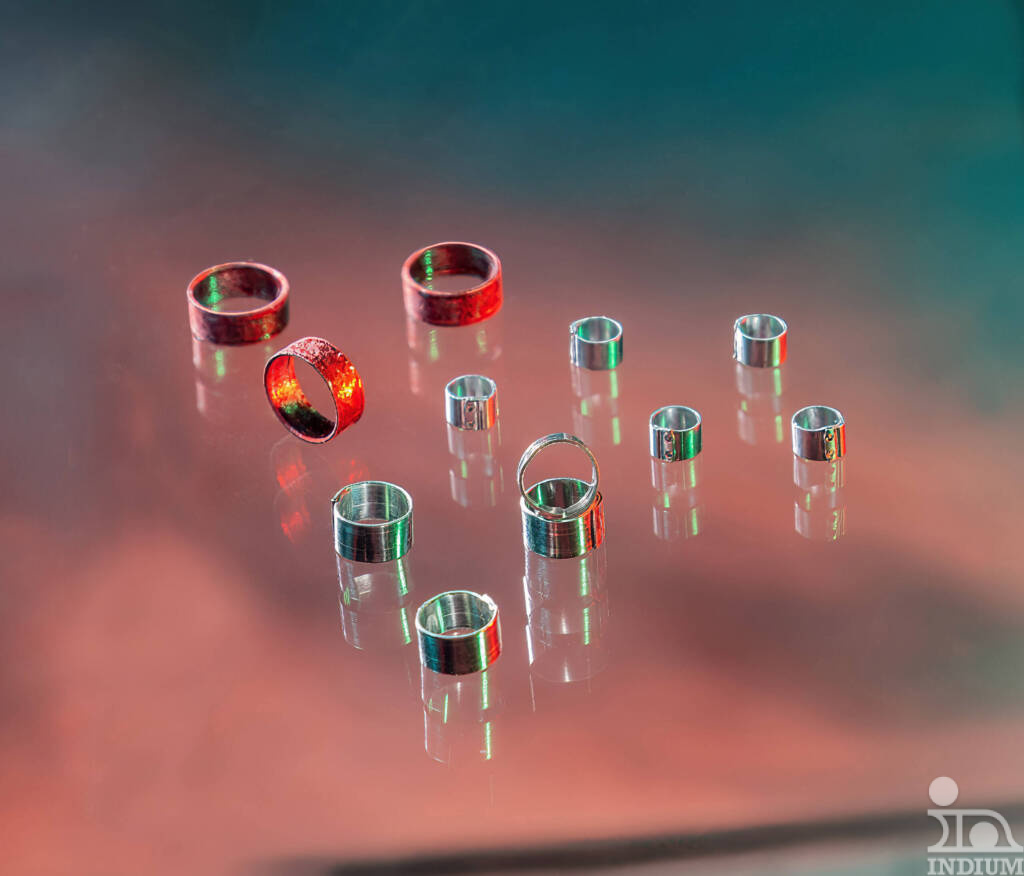 Varios anillos brillantes, unos rojos y otros plateados, colocados sobre una superficie reflectante con un fondo de colores, que recuerdan la precisión de la artesanía del tubo de soldadura.