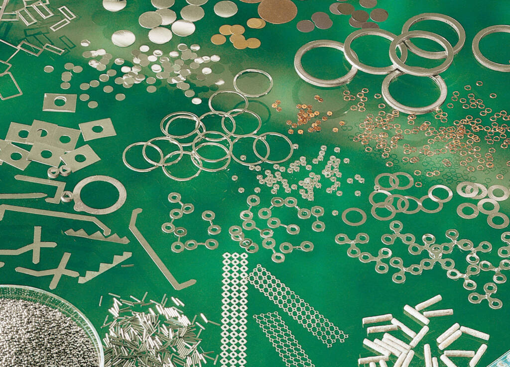 Flux coated solder preforms and assorted small metal components, including rings, discs, rods, and wires, are meticulously arranged on a green surface.