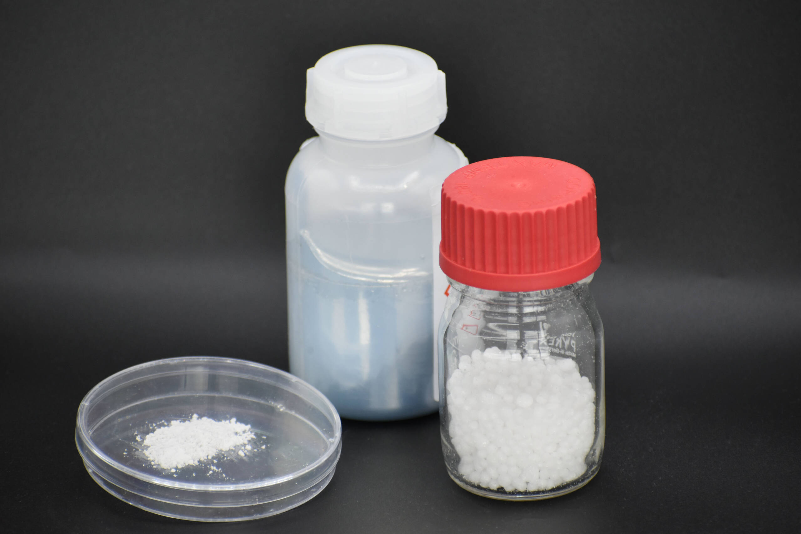 Two jars with white powders, possibly gallium trichloride, and a Petri dish set against a stark black background.