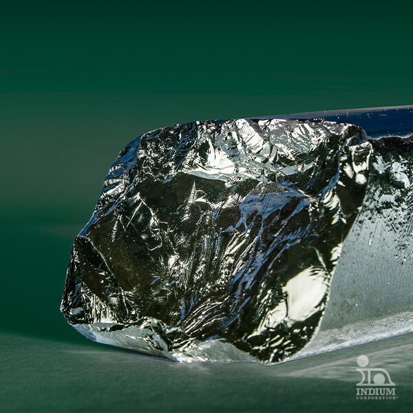 Close-up of a shiny, rough-surfaced gallium metal crystal on a green background.
