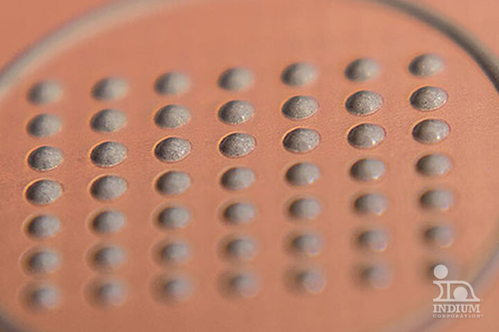 Close-up of a textured surface resembling MEMS chips, with a grid of raised circular bumps on a copper-colored background.