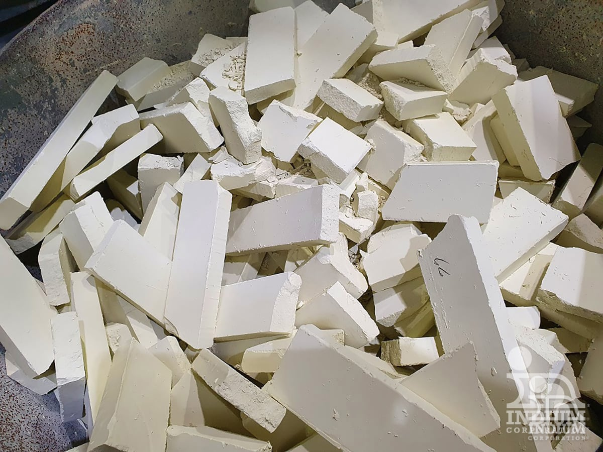 Chunks of white material stacked in a container, featuring a recycling logo in the bottom right corner.