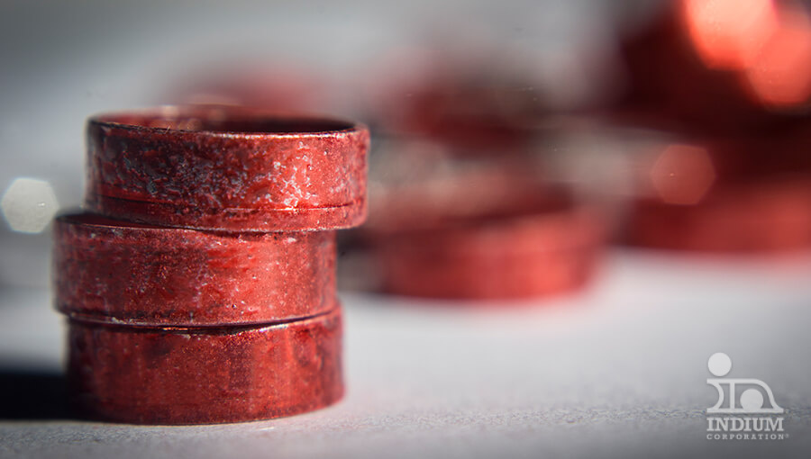 A close-up of three red rusty metal rings stacked on a light gray surface with more rings blurred in the background.
