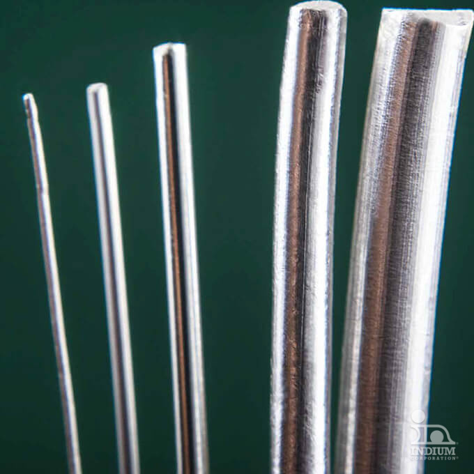 Close-up of five metal rods of varying thickness set against a dark green background.