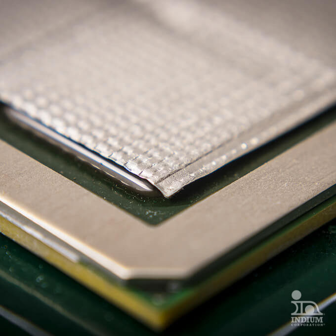 Close-up of a metallic layered structure with textured surfaces and defined edges, possibly part of electronic hardware, against a blurred background.