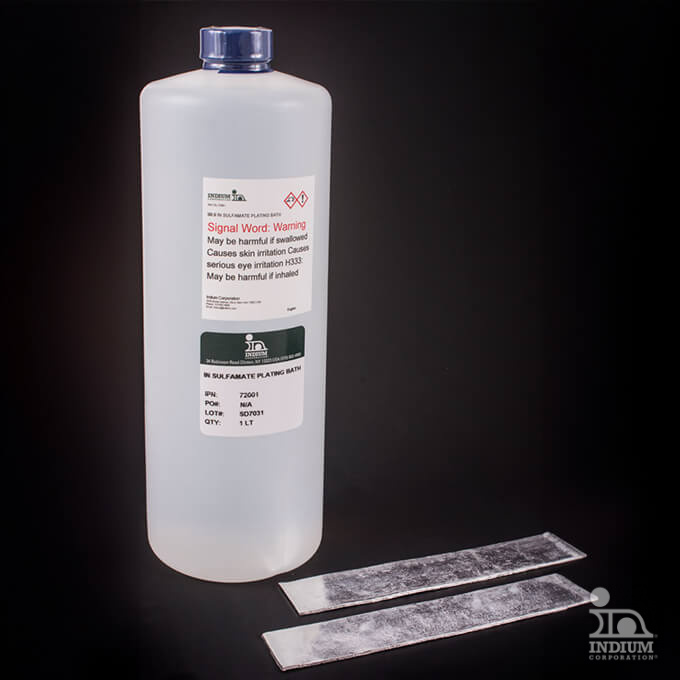 A clear 1-liter chemical bottle with a warning label is placed upright. Two silver metal strips lie beside it on a black surface.
