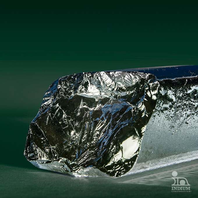 A close-up of a shiny metallic crystal with textured, irregular surfaces against a green gradient background.