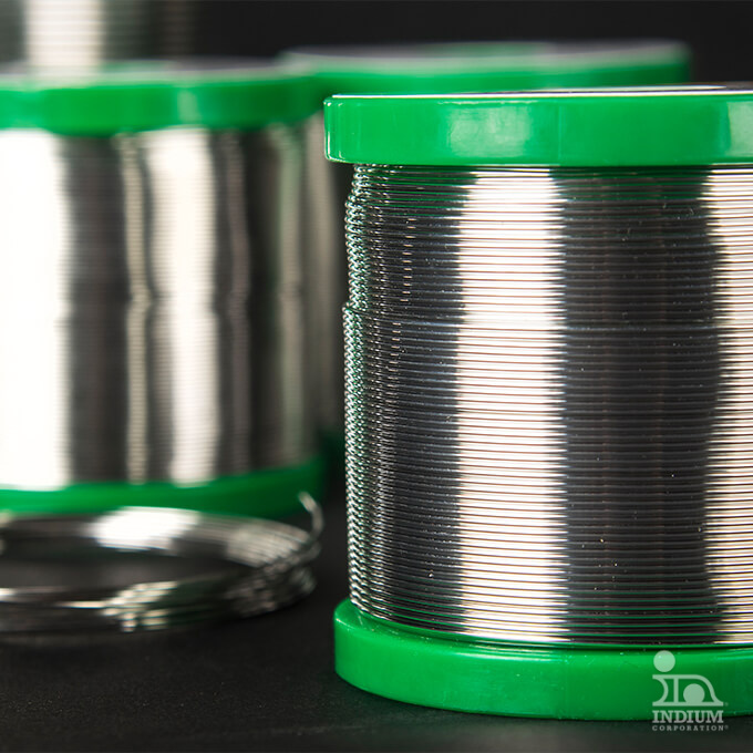 Close-up of spools of shiny metal wire with green plastic tops, standing upright against a dark background.