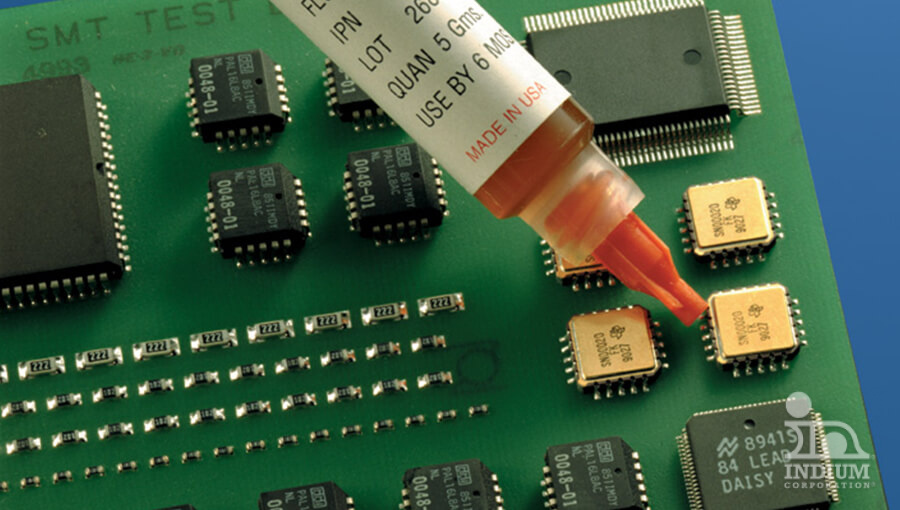 A circuit board with multiple small black and gold components is being treated with a brown liquid from a dropper labeled "Made in USA.