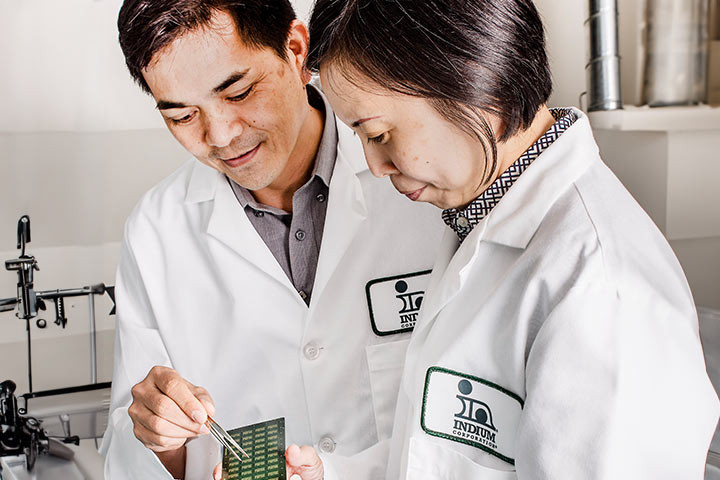 Two people in lab coats examine a circuit board in a laboratory setting.