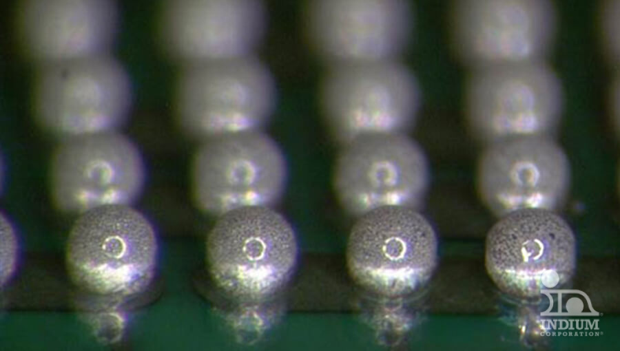 Close-up of rows of small metallic spheres on a green surface, likely part of an electronic component.