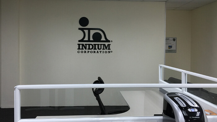 An office cubicle with a chair and desk, featuring the Indium Corporation logo on the wall.