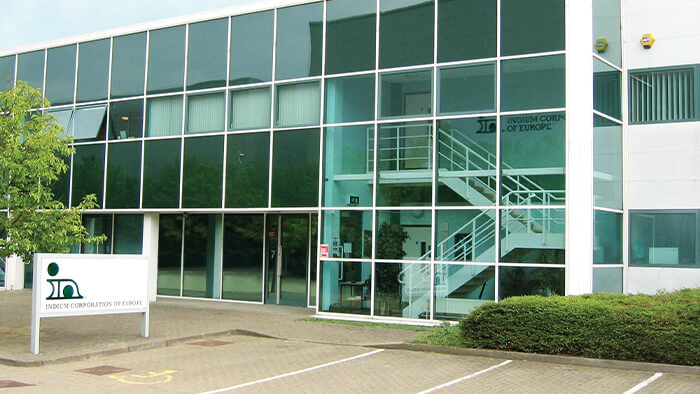 Modern glass office building with sign and trees in the foreground.