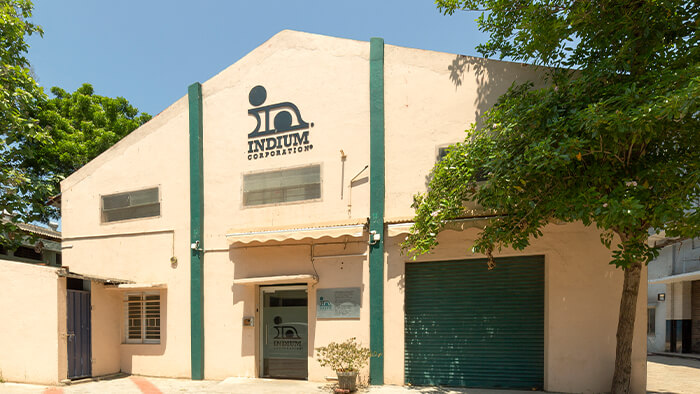 Exterior of a beige Indium Corporation building with green accents and a tree in front.