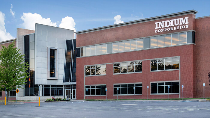 Red-brick building with "Indium Corporation" sign, large windows, and modern design against a blue sky backdrop.