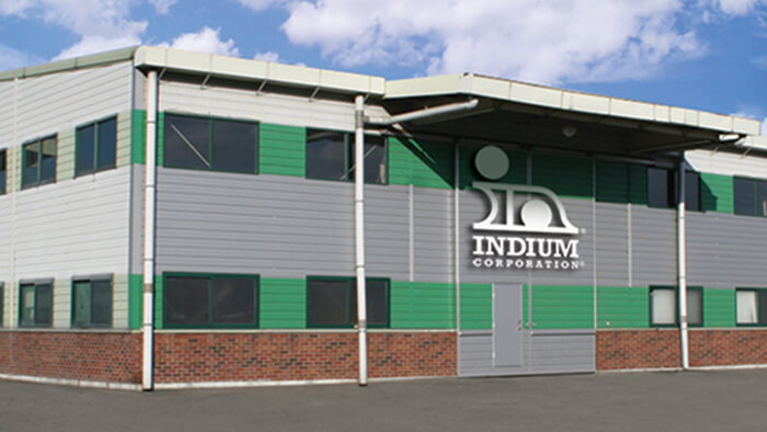 Industrial building with Indium Corporation logo on the facade, featuring green and gray panels under a blue sky.