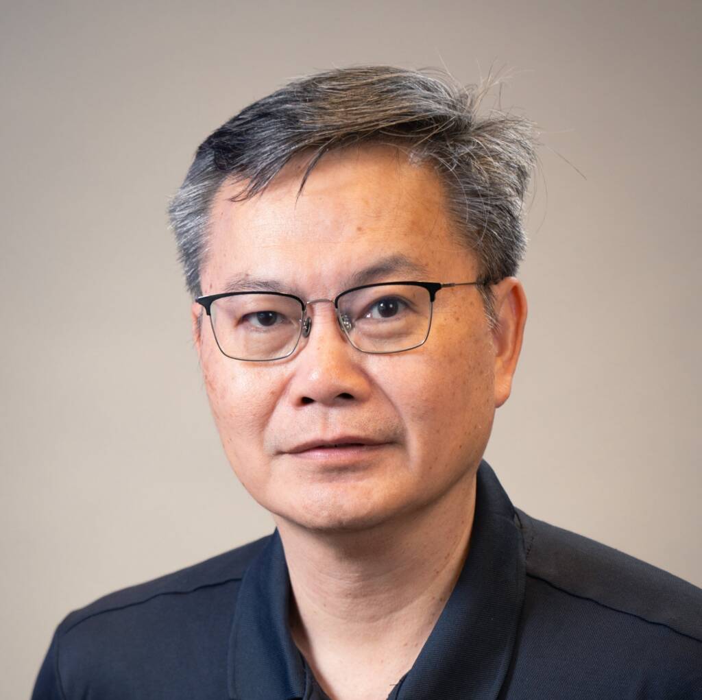 Man with gray hair and rectangular glasses wearing a navy polo shirt with a white embroidered logo.